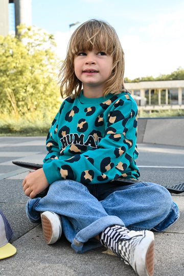 un jeune garçon style skater assis, portant un baggy en jean et un sweat léopard pour enfant