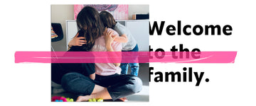 Maman et ses deux enfants, jeunes garçons, faisant un câlin dans leur salon, décoration simple, tableau coloré style street art, blocs de construction colorés au sol, histoire de famille, message "welcome to the family" et scotch décoratif rose fluo sur la photo