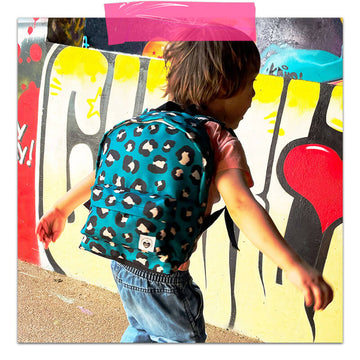 garçon énergique de 3 ans, dans un décor urbain avec graffiti colorés, portant un sac à dos pour enfant motif imprimé léopard