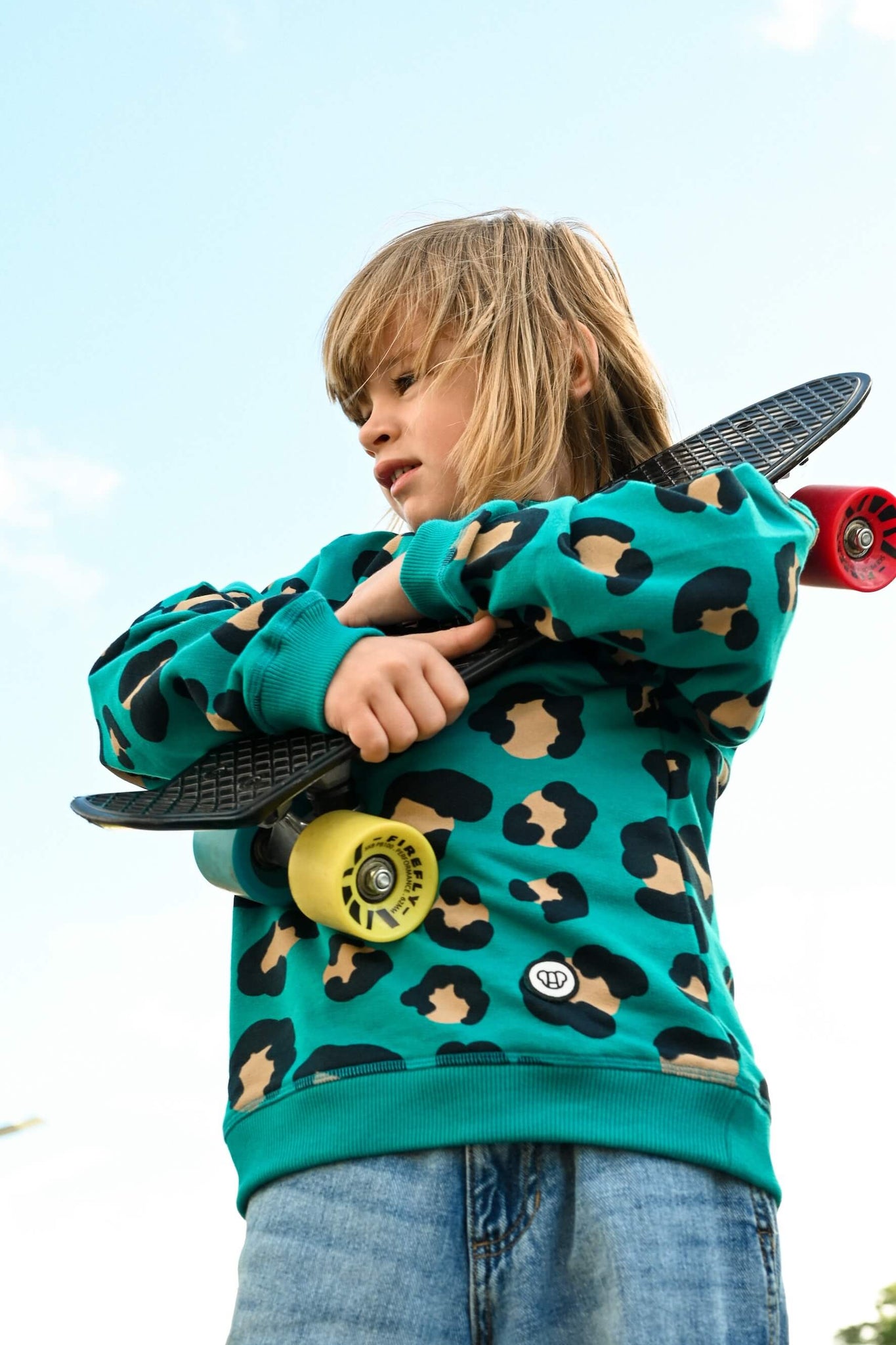 jeune garçon tenant un skateboard et portantun sweat stylé vert avec motif léopard de la marque ALLMEMBERZ