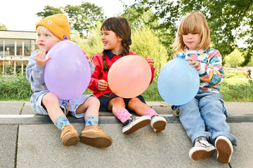 Trois jeunes enfants, deux petits garçons et une petite fille, assis dans un skatepark, look streetwear cool, sweats colorés avec motifs, baggy, short, robe et baskets, ballons colorés
