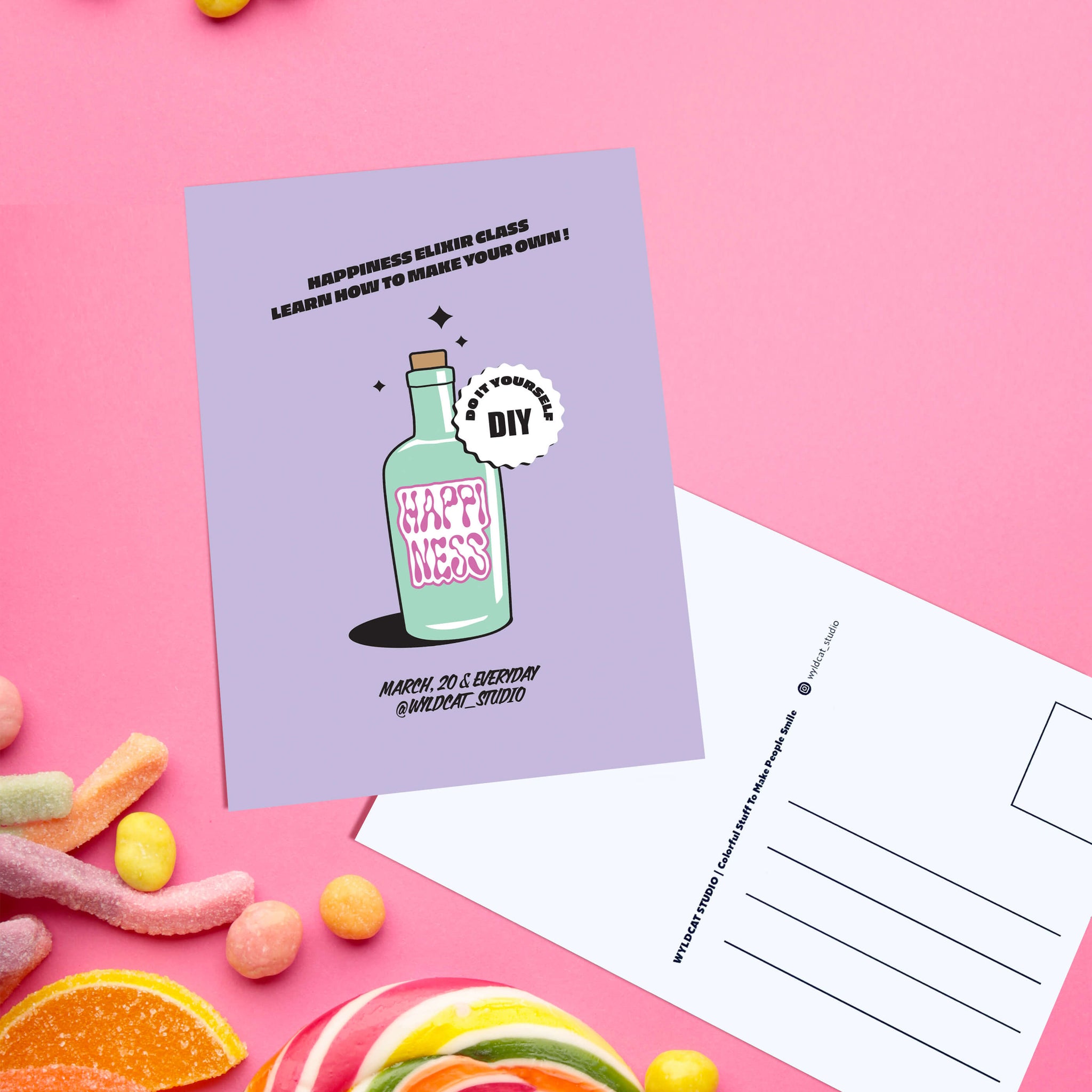 carte postale couleur lilas, message positif Happiness Elixir design flacon rétro, photo sur fond rose avec bonbons