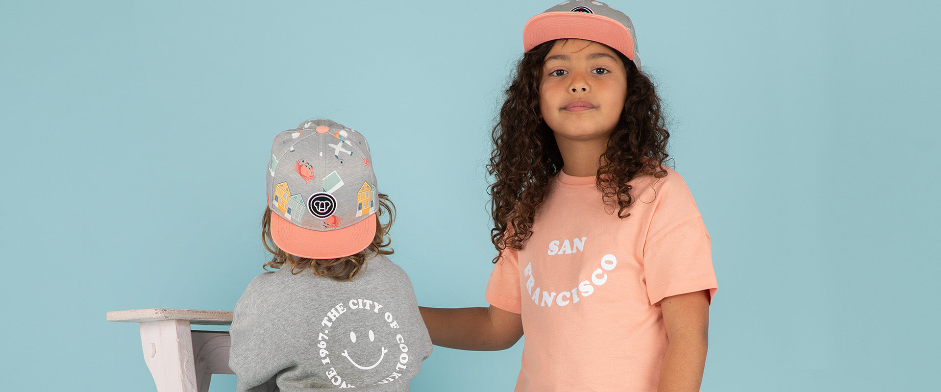 Enfants fille et garçon look streetwear avec t-shirt et sweat cool pour enfants, coupe oversize unisexe en coton bio couleur pêche et gris chiné motif San Francisco, casquettes snapback visière plate motif imprimé, look matchy assorti frère soeur