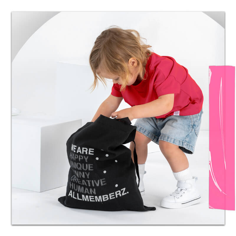petite fille de 2 ans look cool portant un t-shirt rouge et un short en jean bleu, avec un sac en toile noir à motif typo graphique et positif