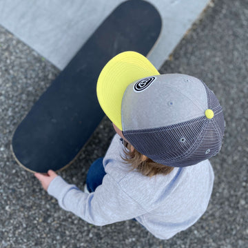 enfant de 2 ans avec un skateboard portant une casquette cool pour enfant, réglable, snapback, en coton et maille filet, visière plate, grise et visière jaune, logo ours Allmemberz brodé devant