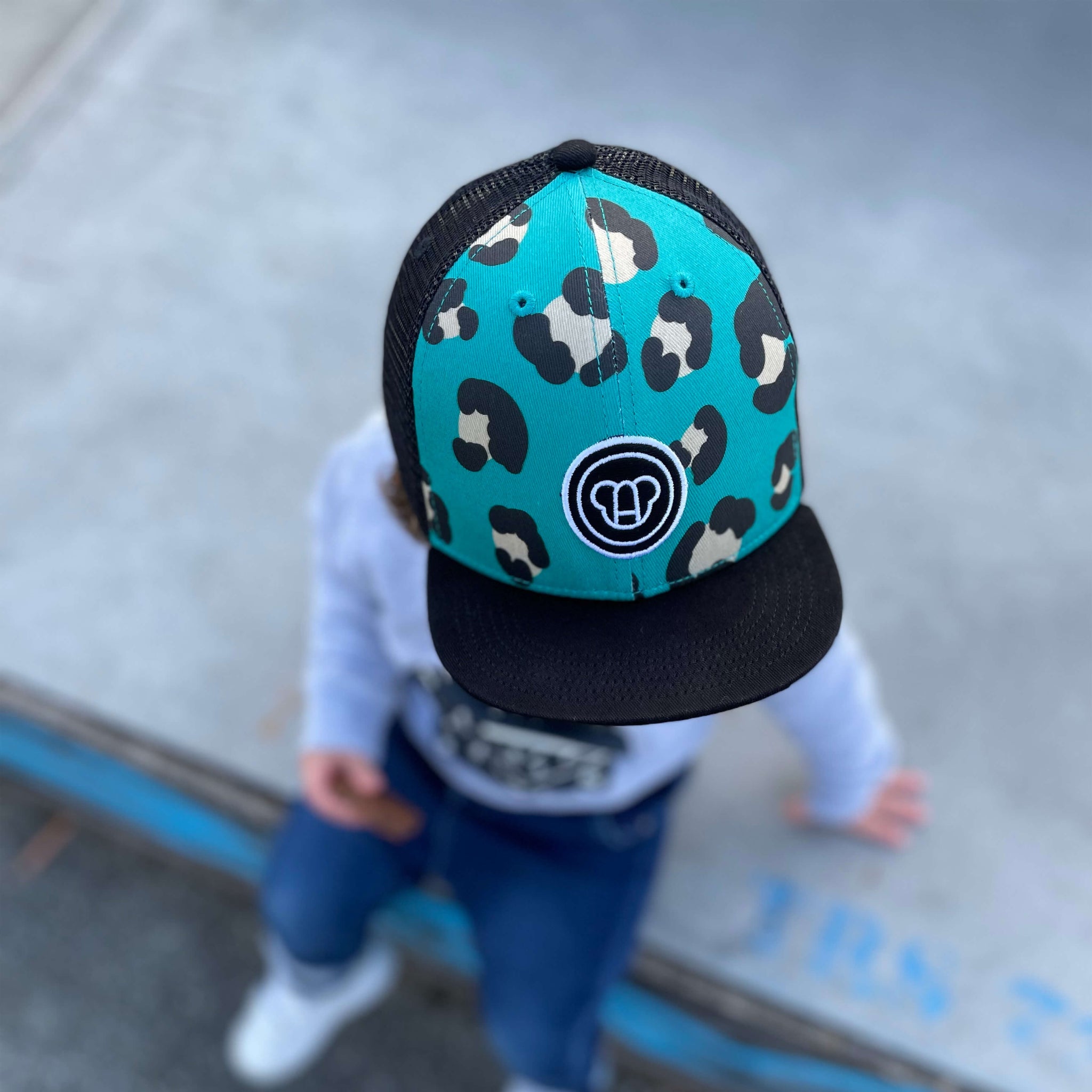 jeune enfant dans un skatepark portant une casquette cool pour enfant, réglable, snapback, en coton et maille filet, visière plate, motif imprimé léopard bleu vert, visière noire, logo ours Allmemberz brodé devant